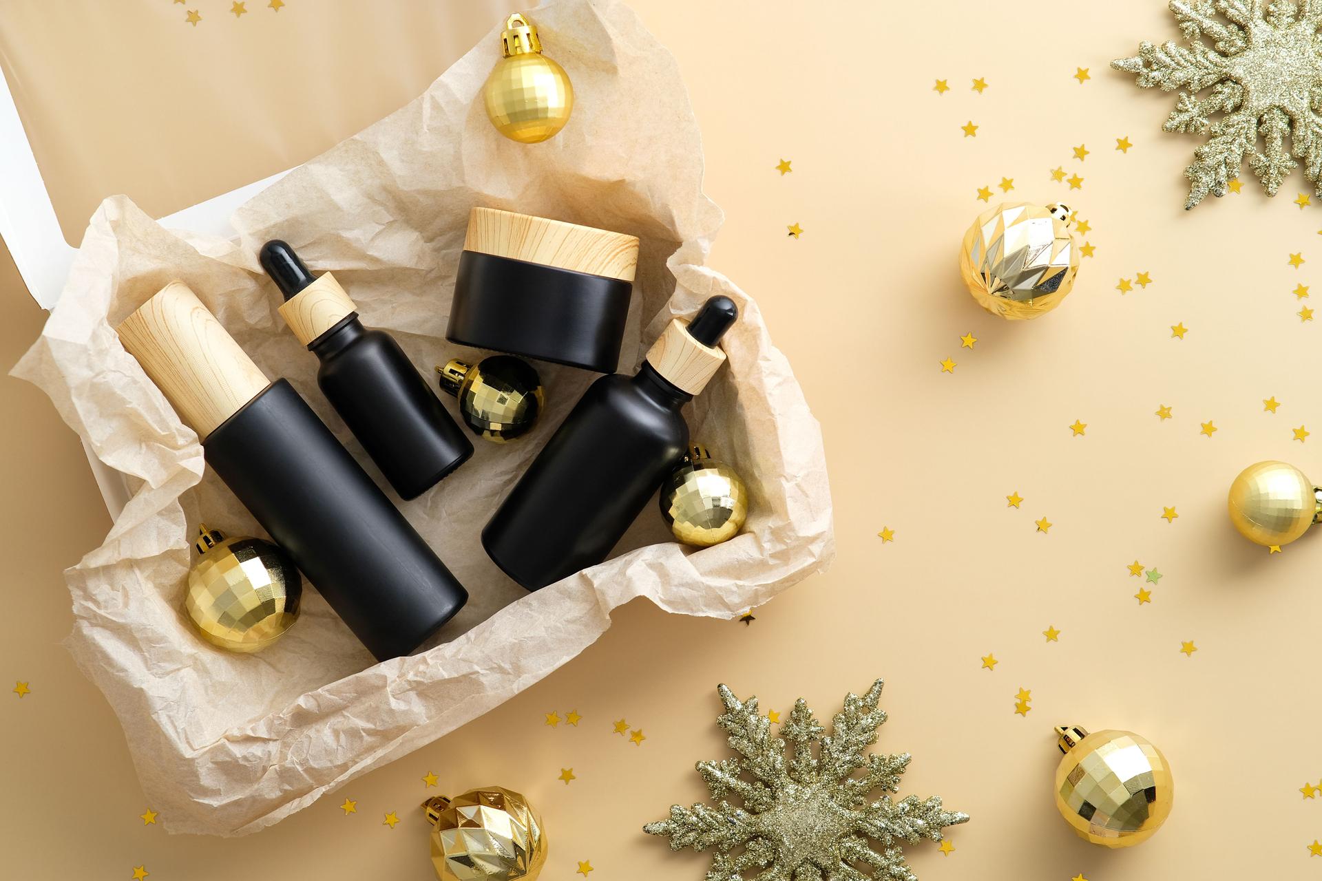 Beauty Subscription Box avec cosmétiques SPA de bain et boules de Noël dorées sur fond beige pastel. Pose plate, vue de dessus.